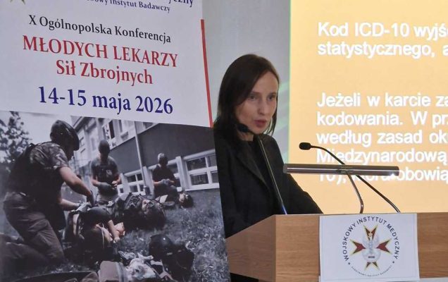 Agata Michalska przy mównicy. Obok niej plakat konferencyjny, za jej plecami na wielkim ekranie wyświetlony slajd z prezentacji.