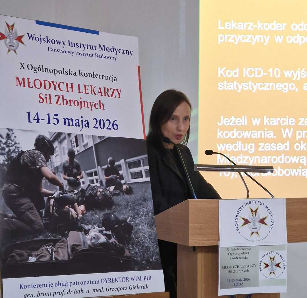 Agata Michalska przy mównicy. Obok niej plakat konferencyjny, za jej plecami na wielkim ekranie wyświetlony slajd z prezentacji.
