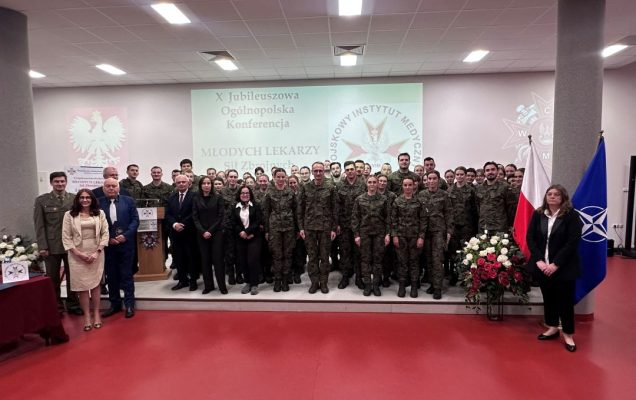 Zdjęcie grupowe uczestników konferencji, za ich plecami wyświetlona plansza z nazwą konferencji i logotypem WIM.