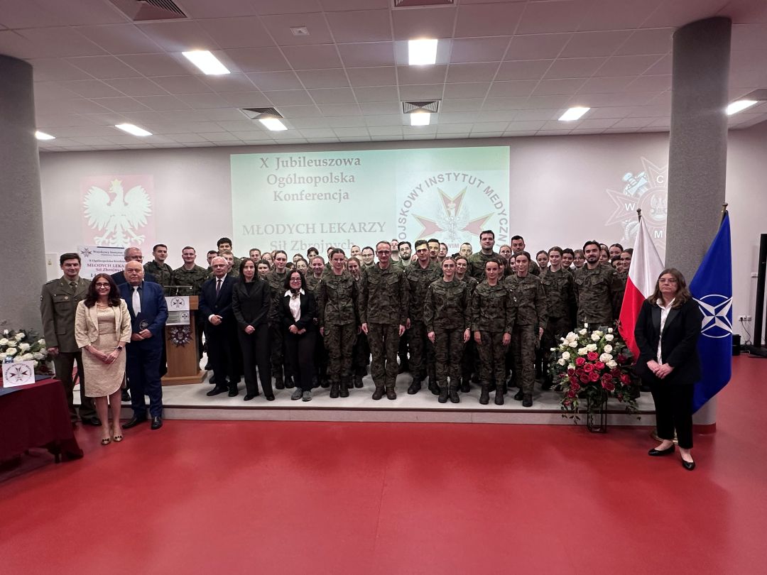 Zdjęcie grupowe uczestników konferencji, za ich plecami wyświetlona plansza z nazwą konferencji i logotypem WIM.