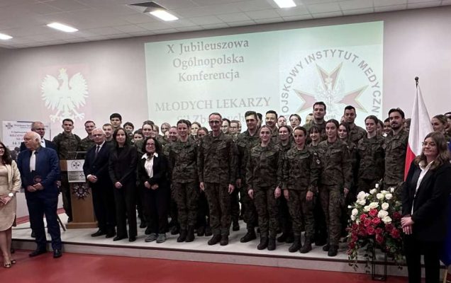 Zdjęcie grupowe uczestników konferencji, za ich plecami wyświetlona plansza z nazwą konferencji i logotypem WIM.