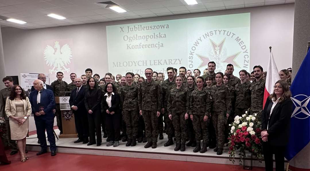 Zdjęcie grupowe uczestników konferencji, za ich plecami wyświetlona plansza z nazwą konferencji i logotypem WIM.