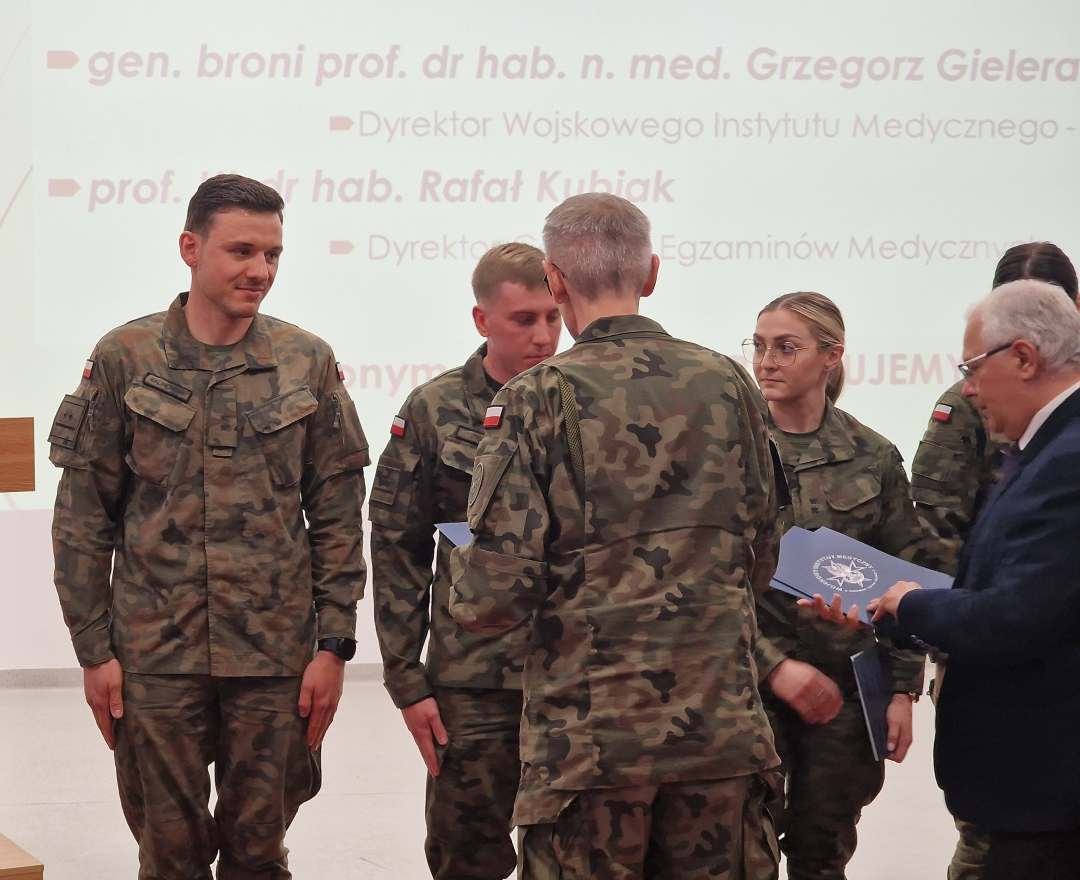 Sala konferencyjna, Dyrektor WIM i Dyrektor CEM wręczają listy gratulacyjne lekarzom w strojach wojskowych.