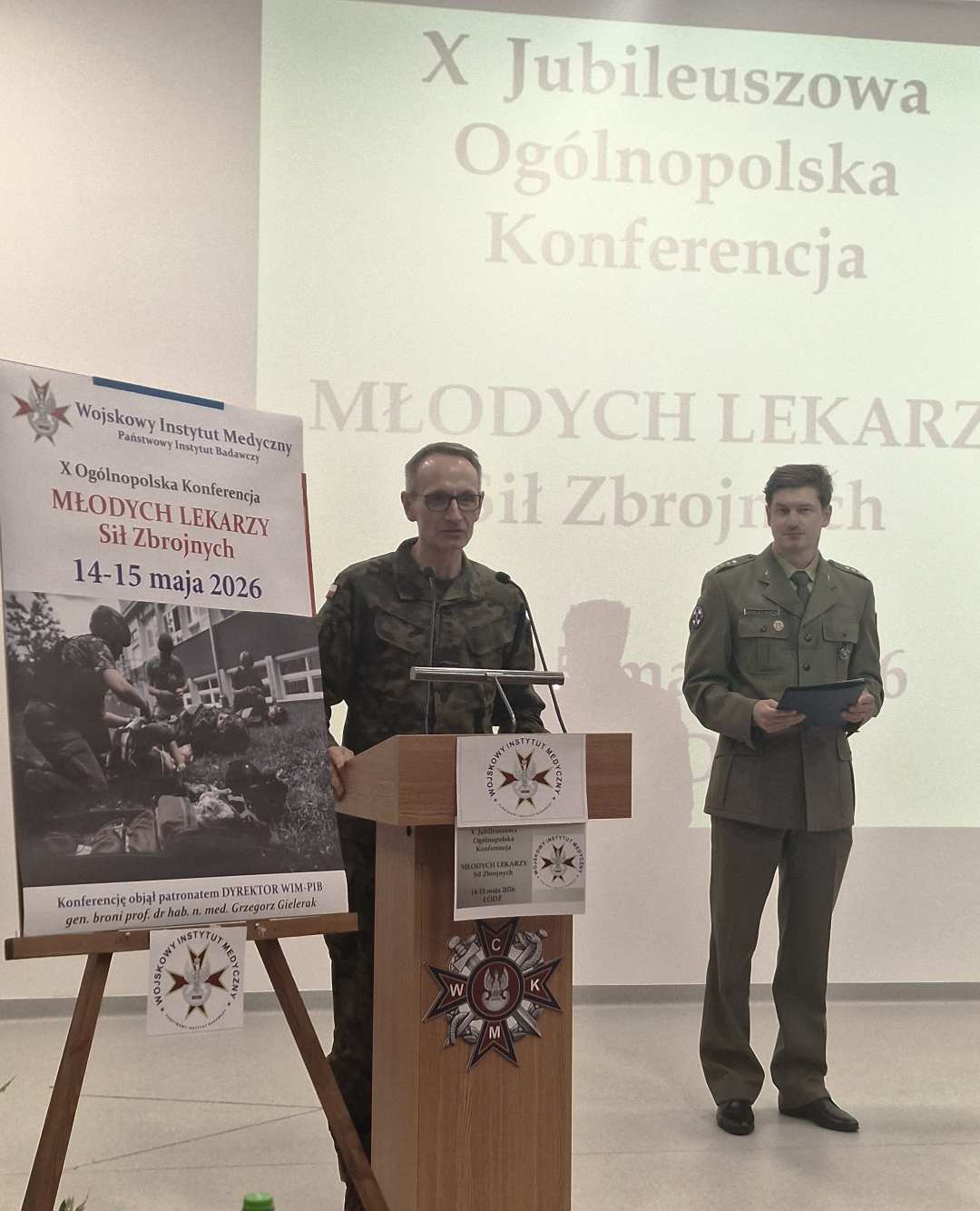 Dyrektor WIM przy mównicy podczas otwarcia konferencji, za jego plecami wyświetlony slajd z konferencji.