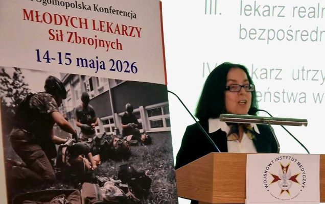 Anna Jaskuła przy mównicy. Obok niej plakat konferencyjny, za jej plecami na wielkim ekranie wyświetlony slajd z prezentacji.