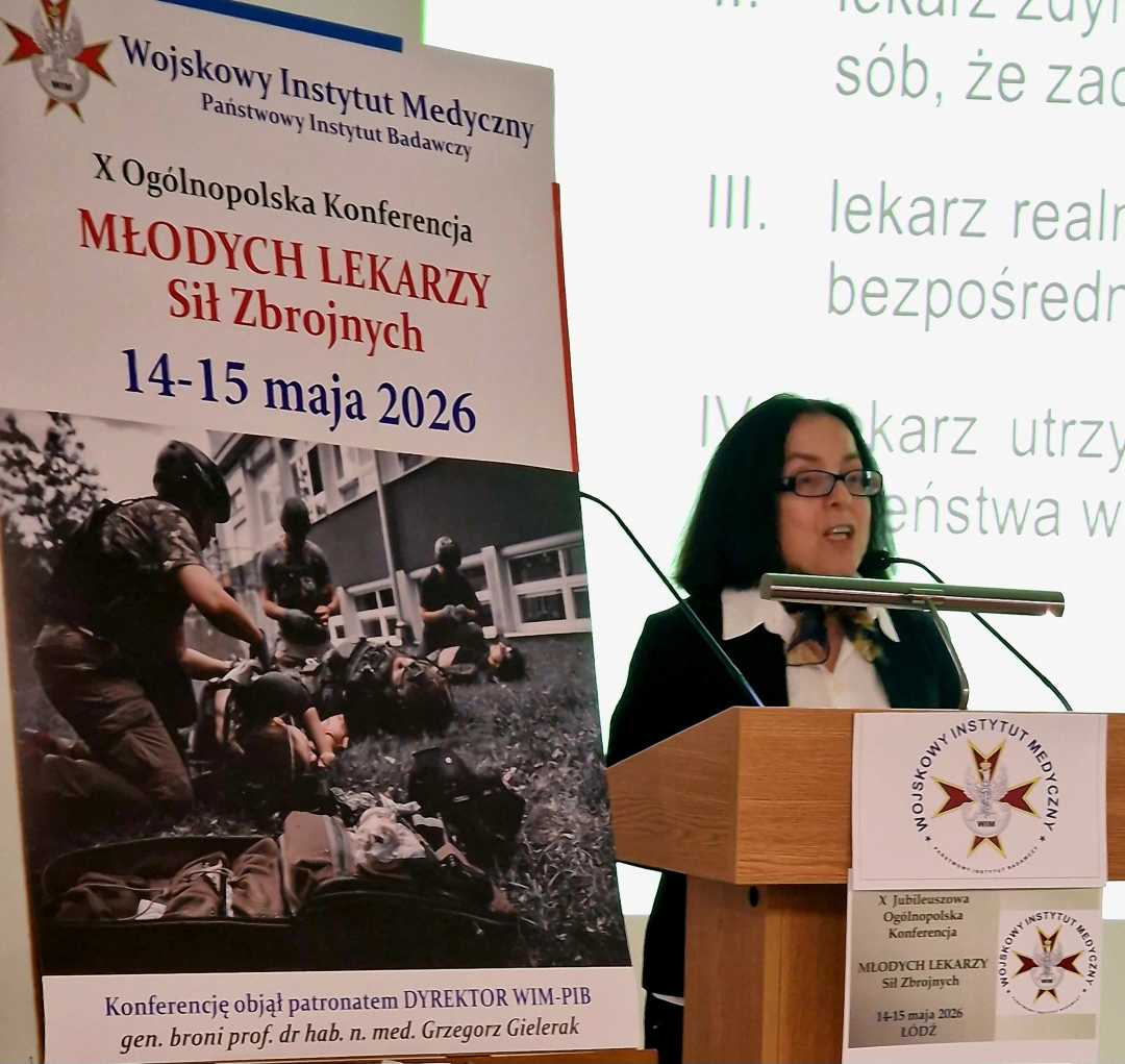 Anna Jaskuła przy mównicy. Obok niej plakat konferencyjny, za jej plecami na wielkim ekranie wyświetlony slajd z prezentacji.