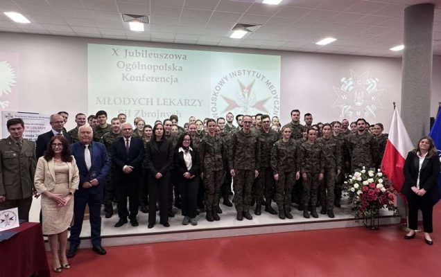 Zdjęcie grupowe uczestników konferencji. Za nimi wyświetlony slajd z nazwą konferencji i logo WIM.