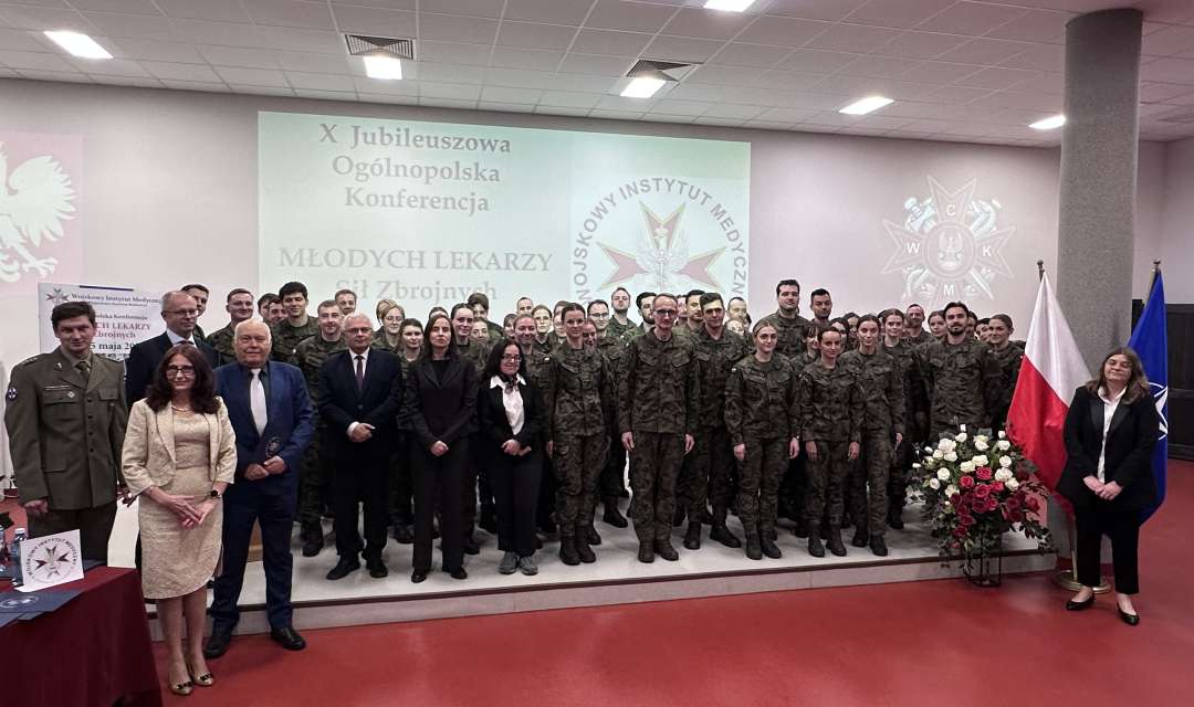 Zdjęcie grupowe uczestników konferencji. Za nimi wyświetlony slajd z nazwą konferencji i logo WIM.