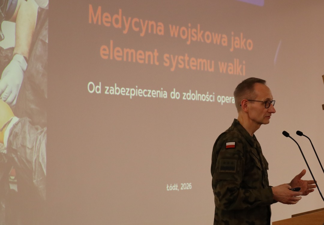 Dyrektor WIM przy mównicy, za jego plecami na ekranie slajd z prezentacji.