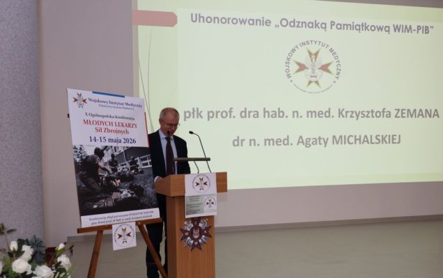 Prelegent przy mównicy, za jego plecami na ekranie slajd z konferencji.