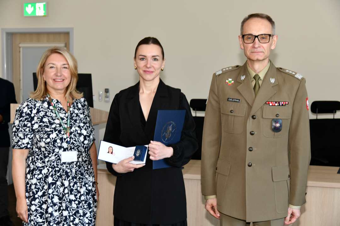 Grzegorz Gielerak i Marta Maciążek pozują z absolwentką stojącą pomiędzy nimi. Kobieta trzyma w rękach dyplom.