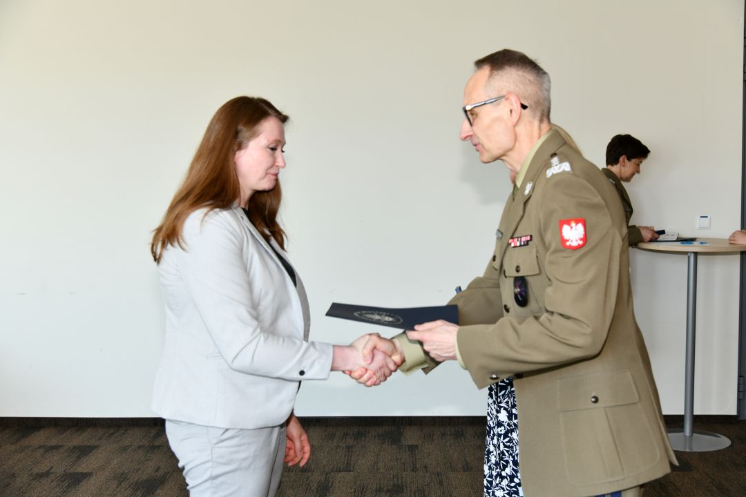 Grzegorz Gielerak ściska dłoń absolwentce i wręcza dyplom, obok stoi uśmiechnięta Marta Maciążek.