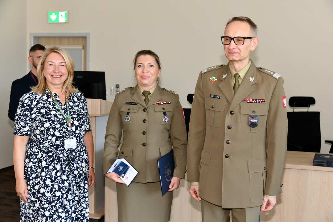 Grzegorz Gielerak i Marta Maciążek pozują z absolwentką w mundur wojskowy stojącą pomiędzy nimi. Kobieta trzyma w rękach dyplom.