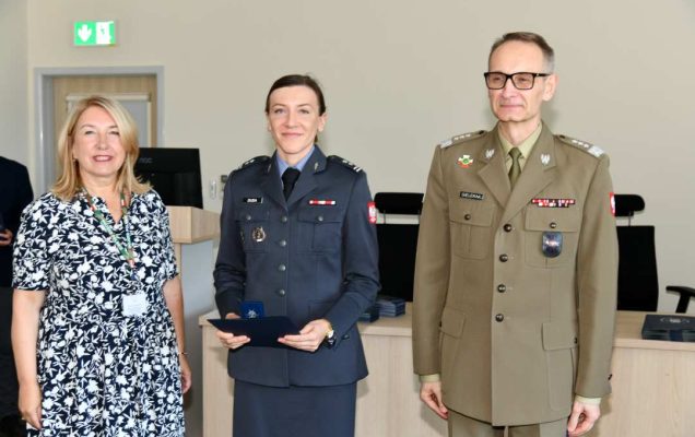 Grzegorz Gielerak i Marta Maciążek pozują z absolwentką ubraną w granatowy mundur stojącą pomiędzy nimi. Kobieta trzyma w rękach dyplom.
