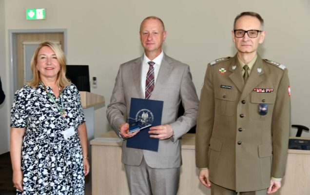 Grzegorz Gielerak i Marta Maciążek pozują z absolwentem stojącym pomiędzy nimi. Mężczyzna trzyma w rękach dyplom ukończenia studiów.