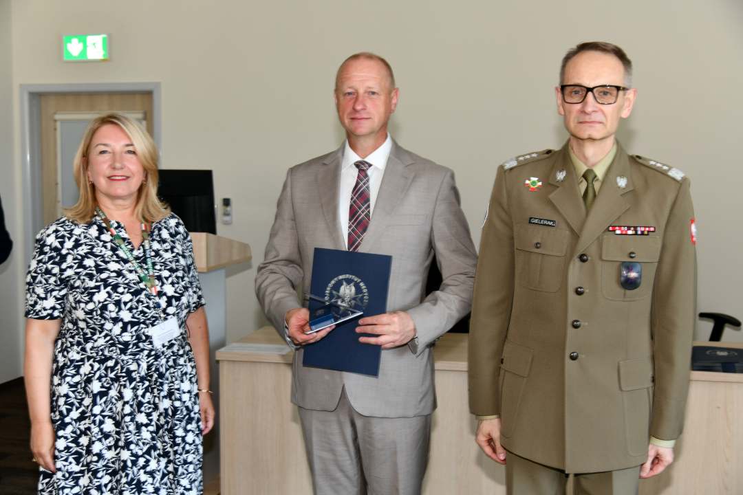 Grzegorz Gielerak i Marta Maciążek pozują z absolwentem stojącym pomiędzy nimi. Mężczyzna trzyma w rękach dyplom ukończenia studiów.