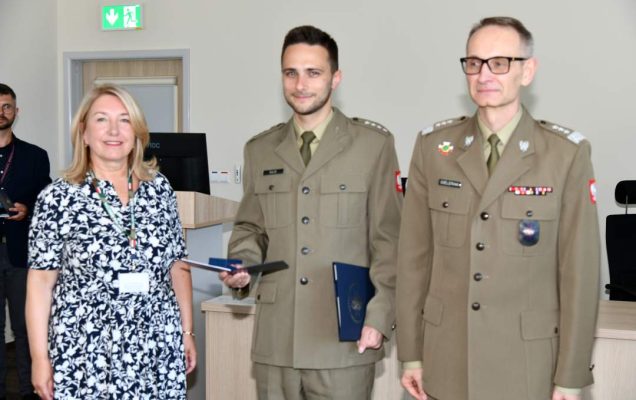 Grzegorz Gielerak i Marta Maciążek pozują z absolwentem stojącym pomiędzy nimi. Mężczyzna ubrany jest w mundur wojskowy, w rękach dyplom ukończenia studiów.