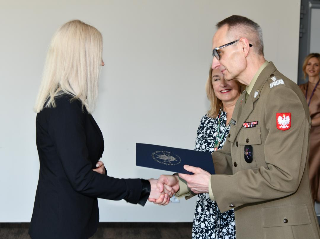 Grzegorz Gielerak ściska dłoń absolwentce odbierającej dyplom, obok stoi uśmiechnięta Marta Maciążek.