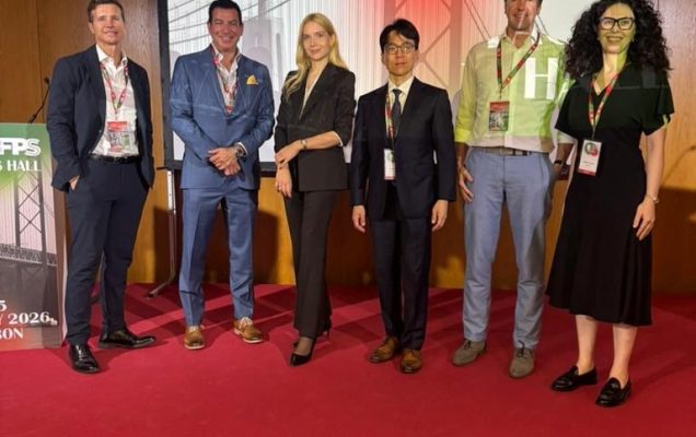 Członkowie WIM pozują do zdjęcia w holu konferencyjnym. Hol pokrywa czerwony dywan, przed pozującymi do zdjęcia stoi kosz z bukietem kwiatów.