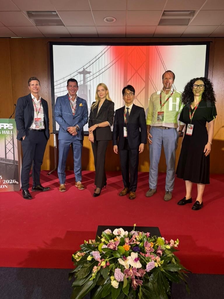 Członkowie WIM pozują do zdjęcia w holu konferencyjnym. Hol pokrywa czerwony dywan, przed pozującymi do zdjęcia stoi kosz z bukietem kwiatów.