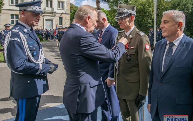 Czesław Mroczek przypina Dyrektorowi WIM medal przed gmachem policji.