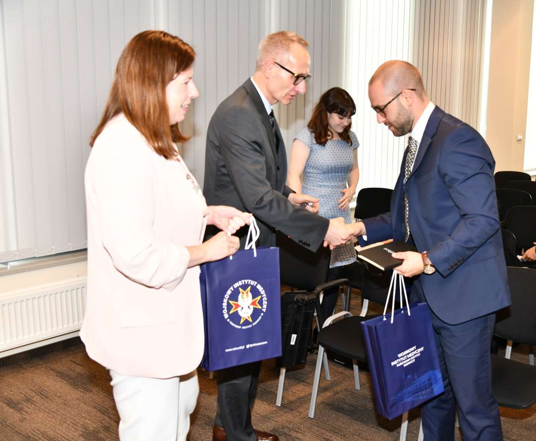 Dyrektor i Komendant WIM przekazują gościom upominki.